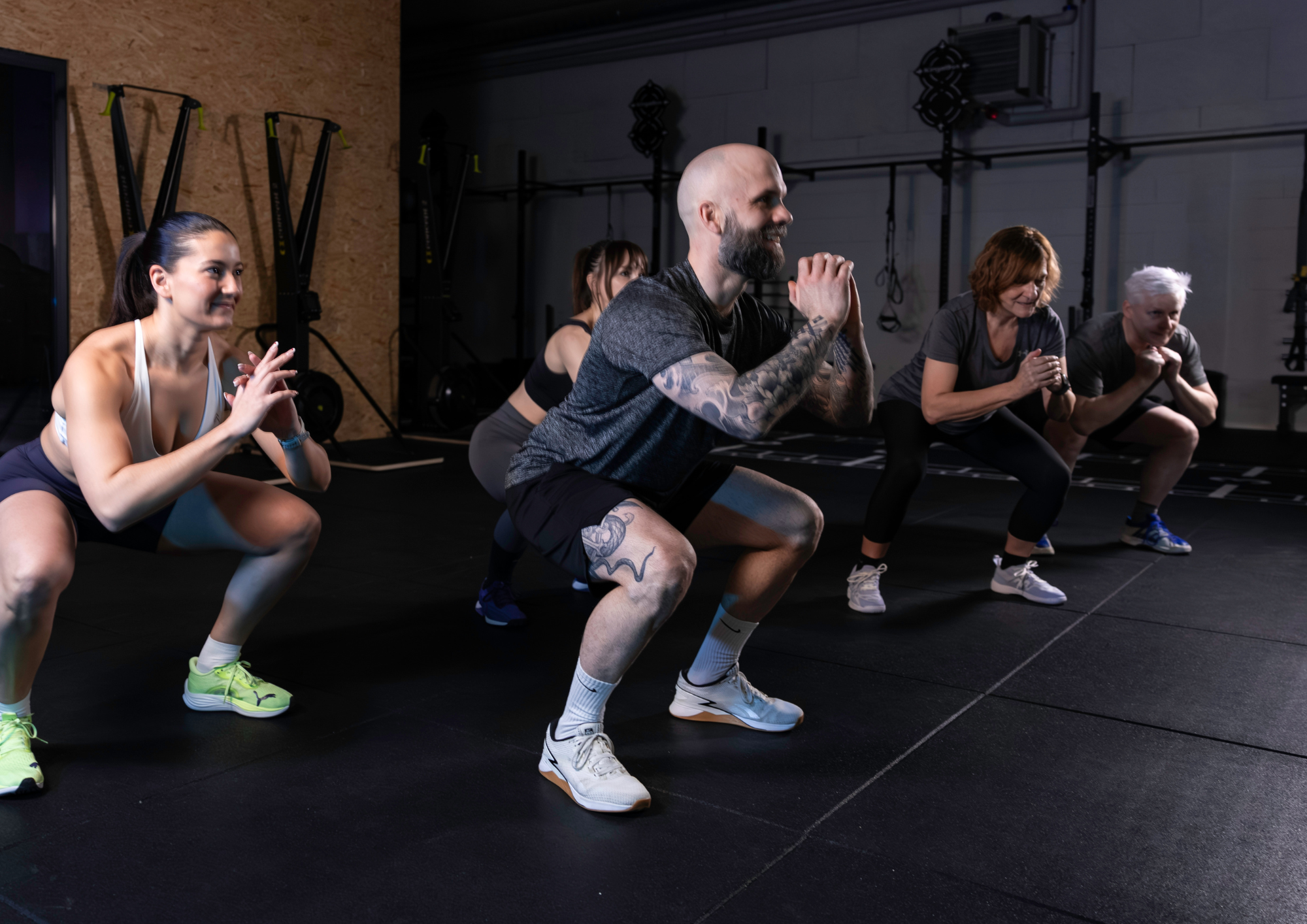 Group of diverse people aged 35-50 high-fiving after a workout session in a functional gym, sweating but smiling, showing camaraderie. No clearly identifiable faces.