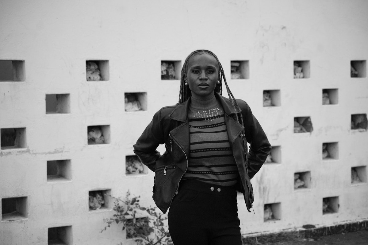 A young woman stands in front of a patterned wall.