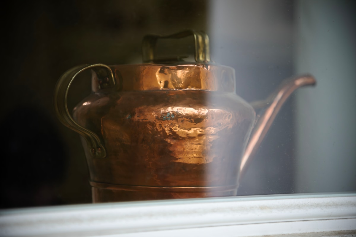 A vintage copper teapot on a windowsill.