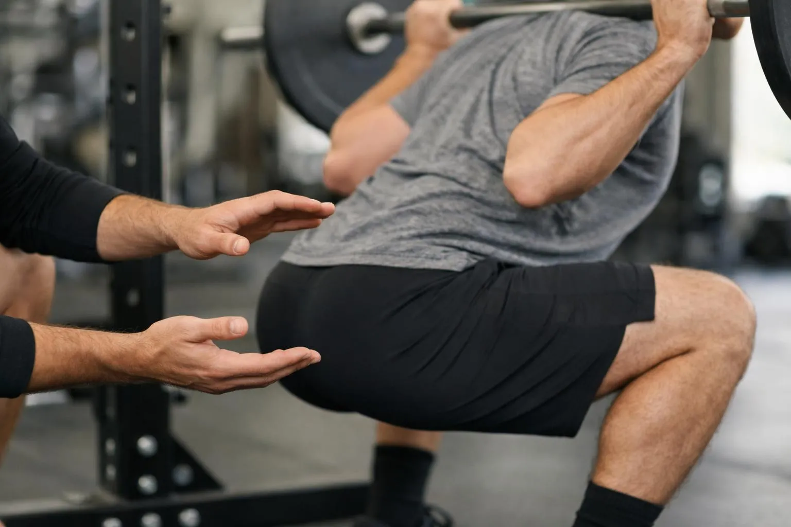 Coach diplômé analysant la posture d'un athlète masculin de 40 ans effectuant un mouvement de squat dans une salle d'entraînement fonctionnel équipée de racks et kettlebells, le coach tenant une tablette pour noter les observations, éclairage professionnel, visages flous