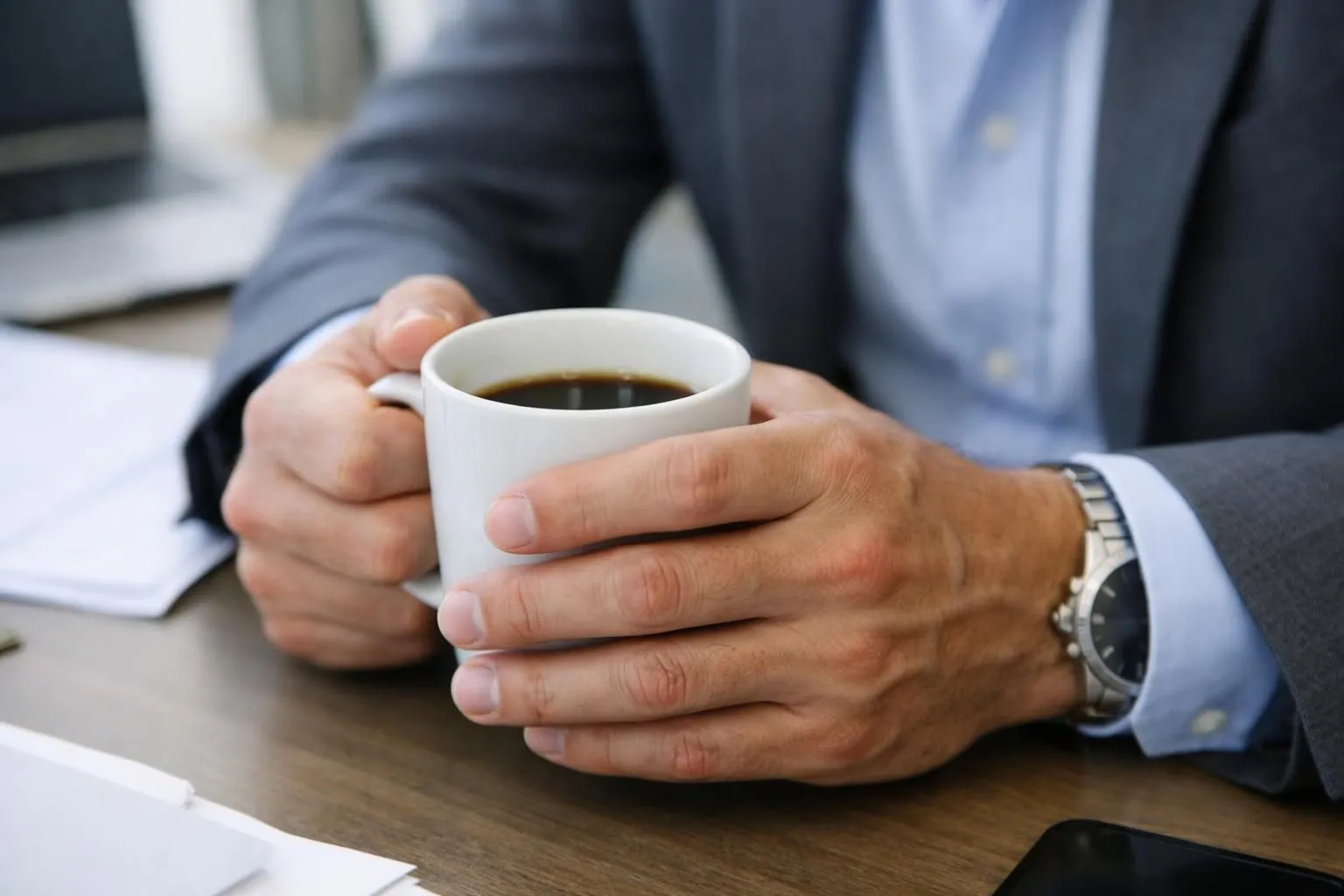 Un homme d'environ 40 ans dans une cuisine moderne, debout devant un comptoir, tenant uniquement une tasse de café, regardant sa montre avec un air pressé, lumière matinale naturelle, visage flouté, style documentaire professionnel, aucun texte visible