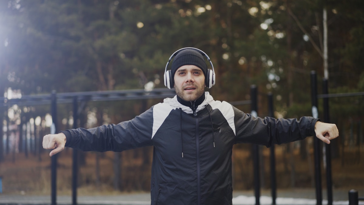 Homme en veste noire et casque d'écoute, dans un parc boisé.