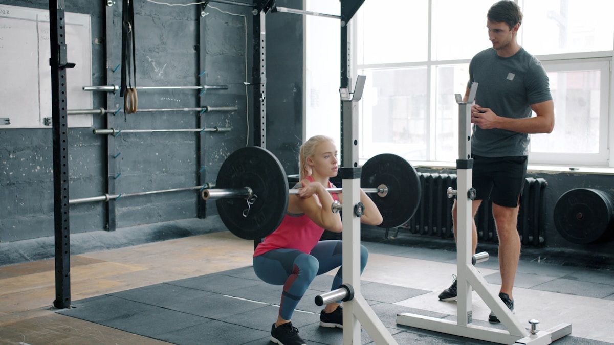 Femme en tenue de sport s'entraînant avec un haltère sous la supervision d'un entraîneur.