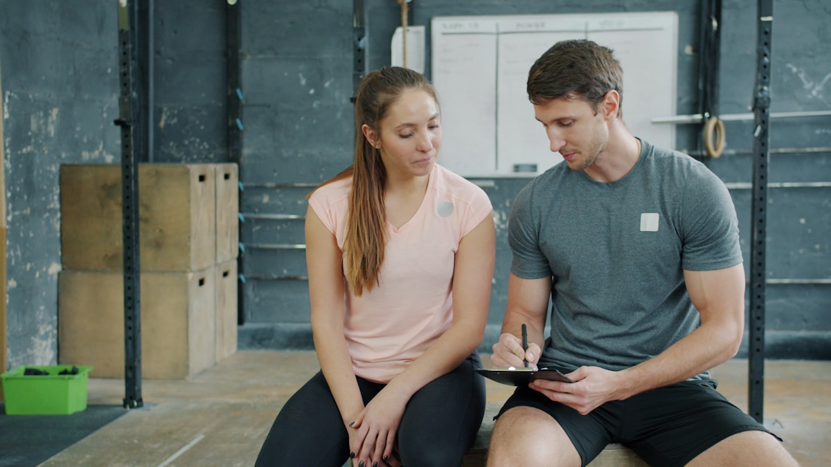 Deux personnes discutent dans un gymnase, l'une tient une tablette.
