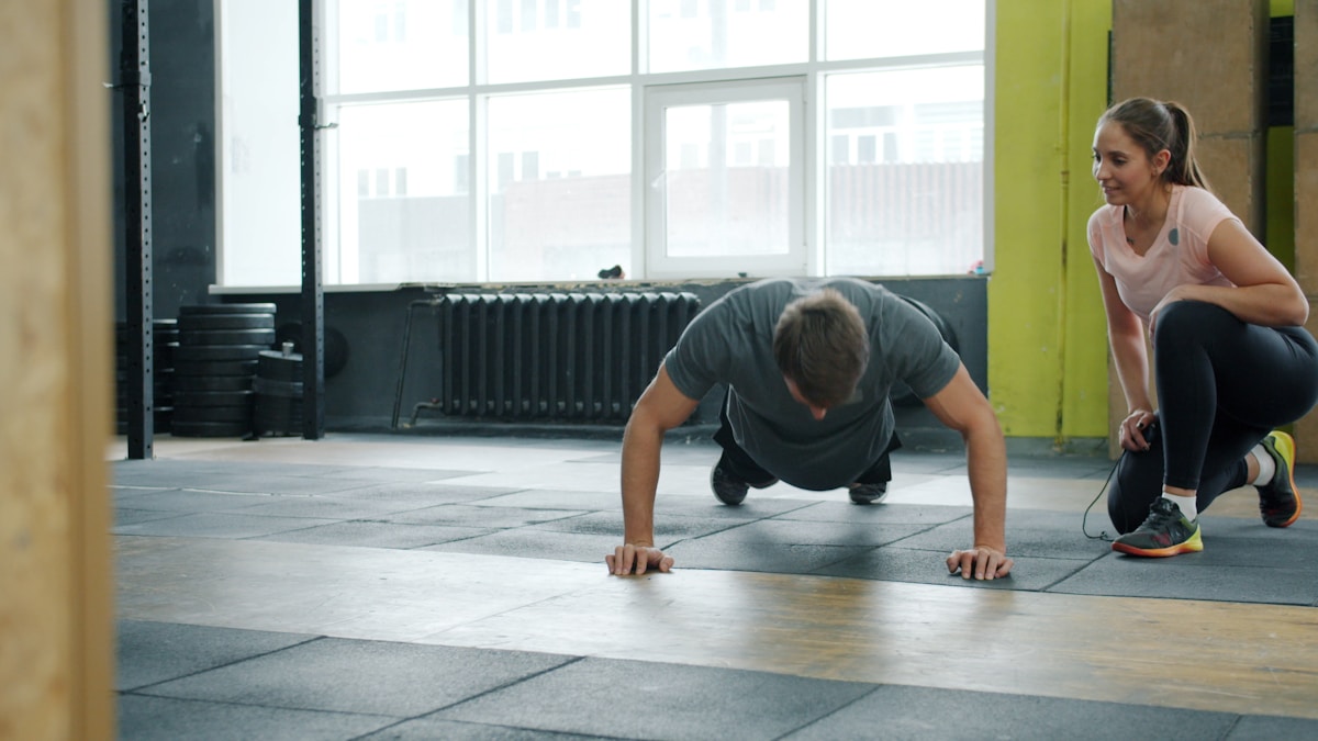 Homme effectuant des exercices de pompes sous la supervision d'une femme dans une salle de gym.