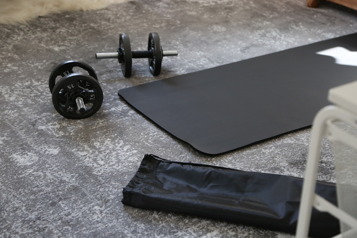 Haltères, tapis d'exercice et équipement de fitness sur sol gris.