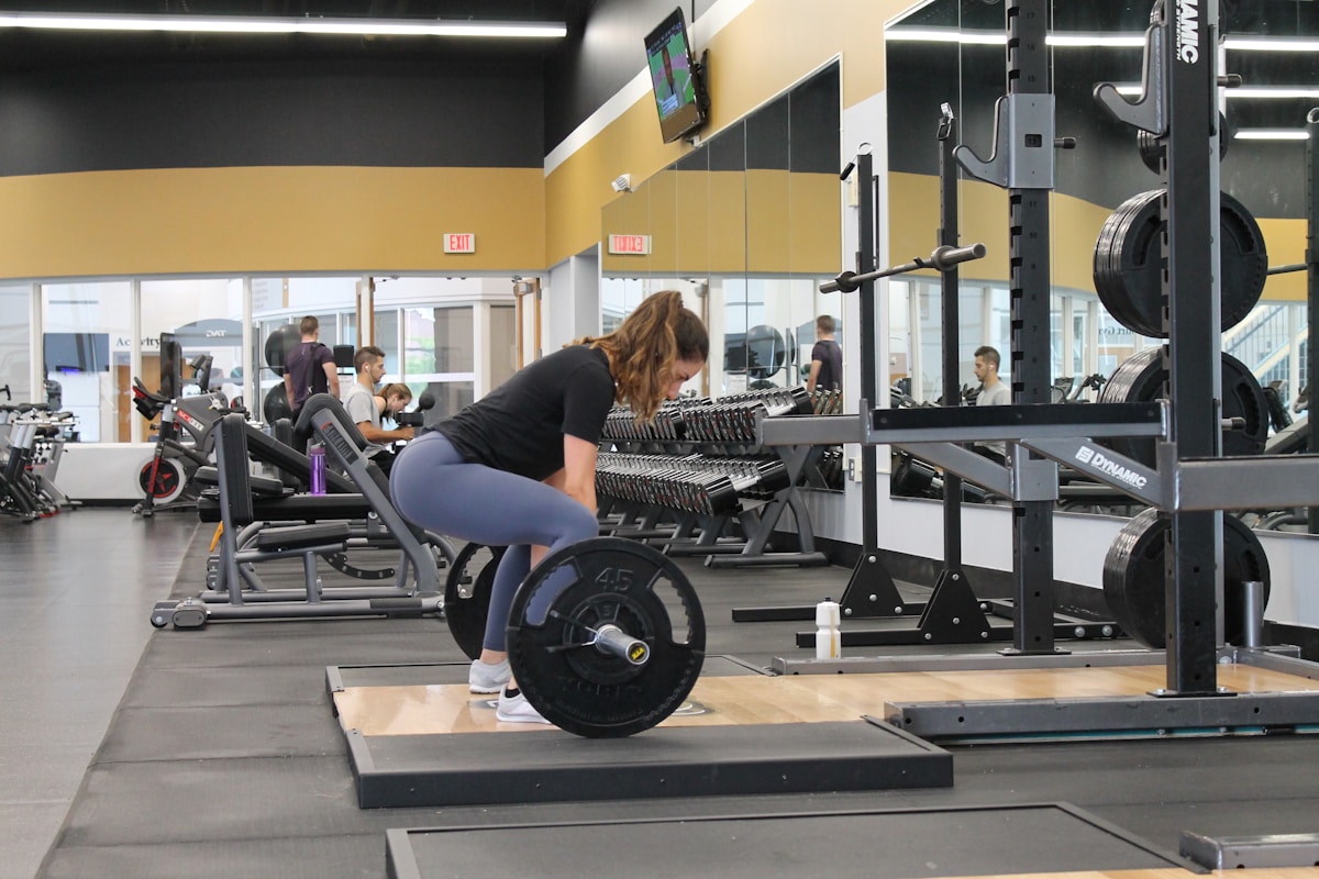 Salle de gym avec équipements de musculation et personnes s'entraînant.