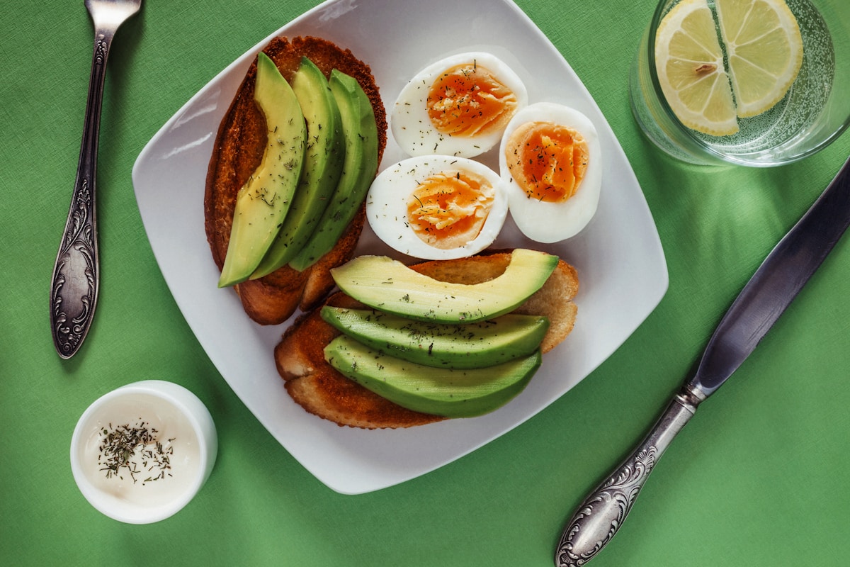 Assiette avec pain, avocats, œufs durs et assaisonnements sur fond vert.