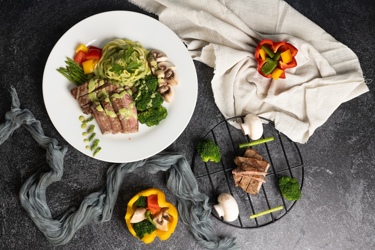 Assiette de viande, légumes et pâtes sur fond sombre.
