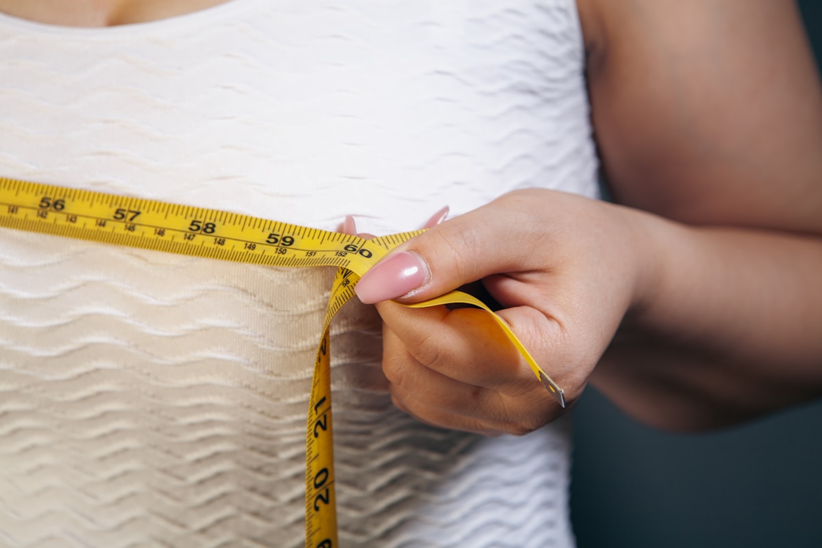 Main féminine mesurant la taille avec un ruban à mesurer.