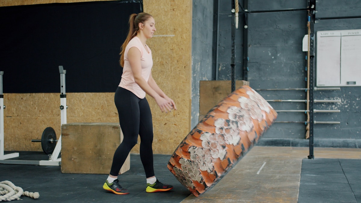 Femme athlétique dans un gymnase, soulevant un gros pneu orange.