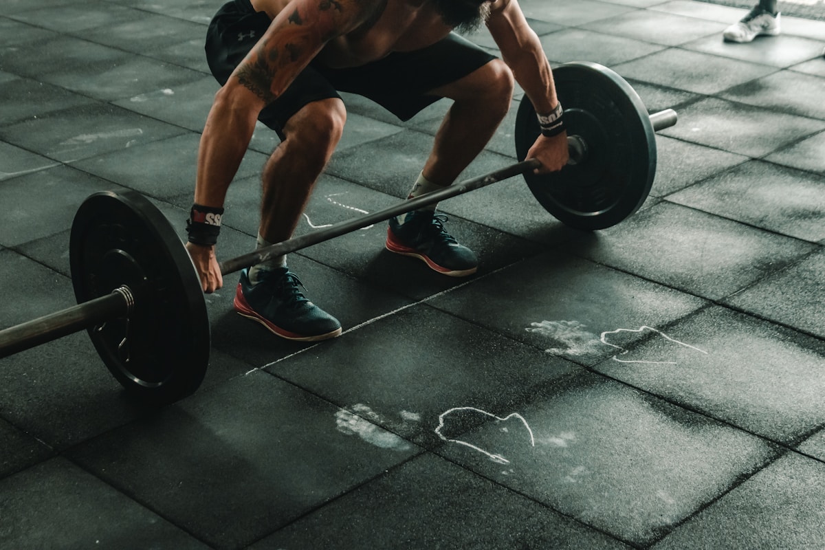 Athlète musclé soulevant un haltère sur un sol de gym.