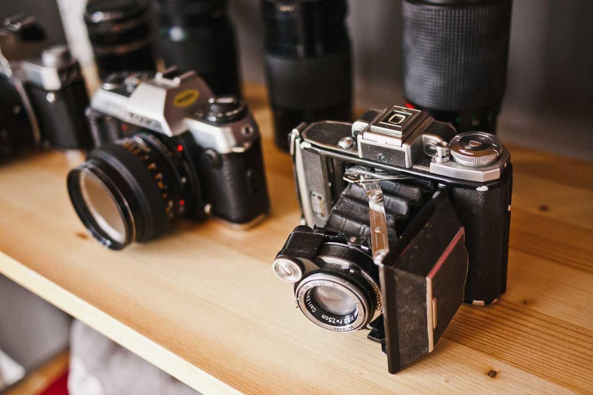 Appareils photo et objectifs vintage sur une étagère en bois.