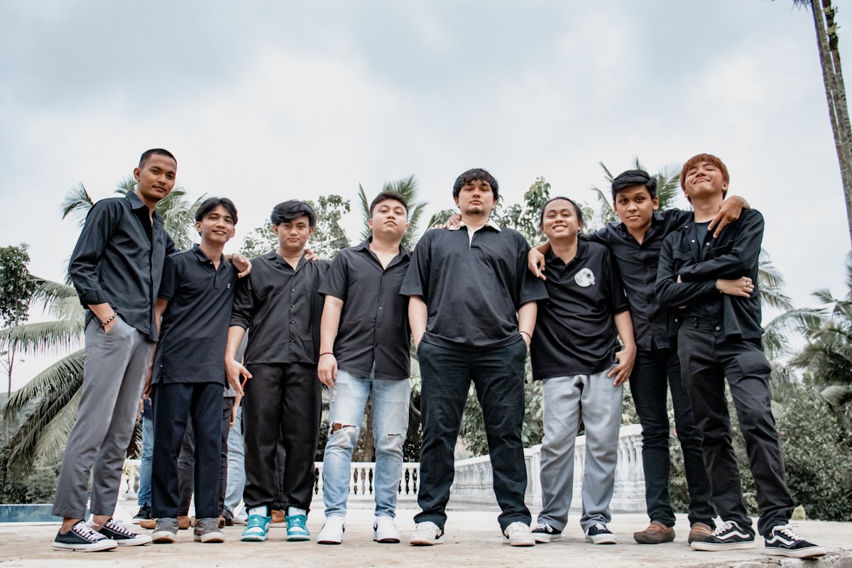 Groupe de jeunes hommes en tenue noire posant ensemble à l'extérieur.
