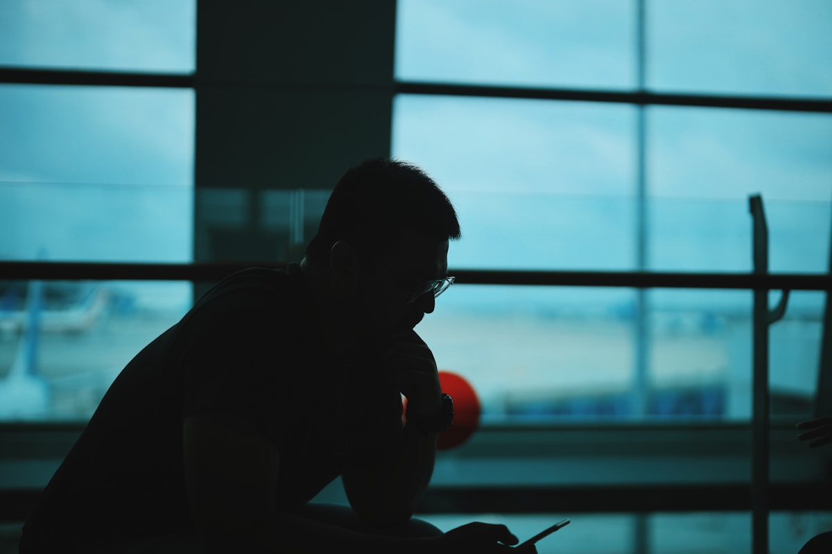Silhouette d'un homme assis devant une fenêtre avec un ciel bleu.