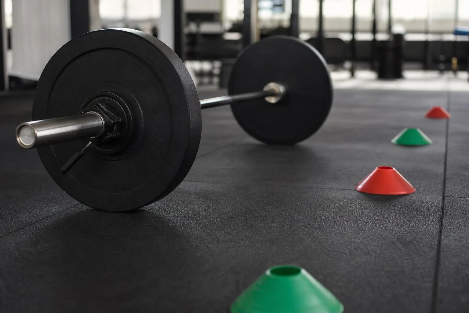 Haltères noirs et cônes colorés sur un sol de fitness.