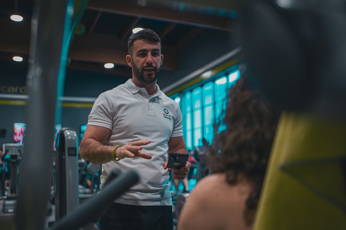 Homme en uniforme blanc parlant avec une personne dans une salle de sport.