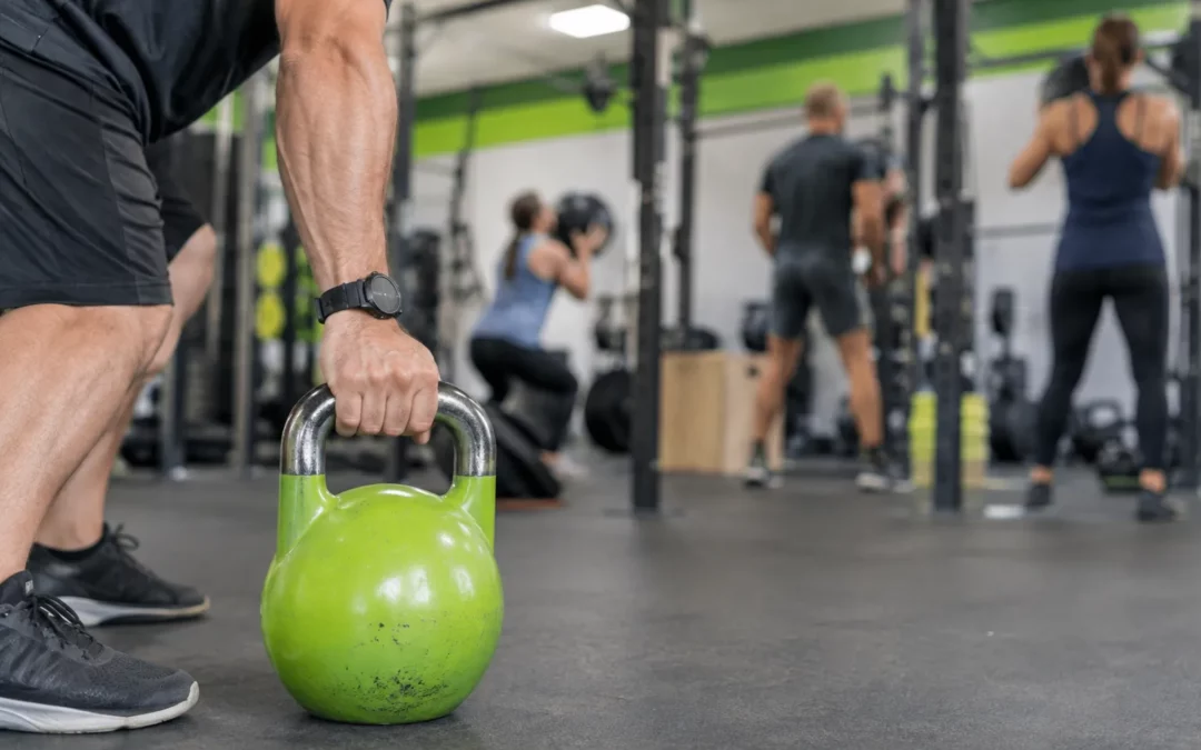 Main de coach tenant une kettlebell verte sur fond de salle CrossFit.