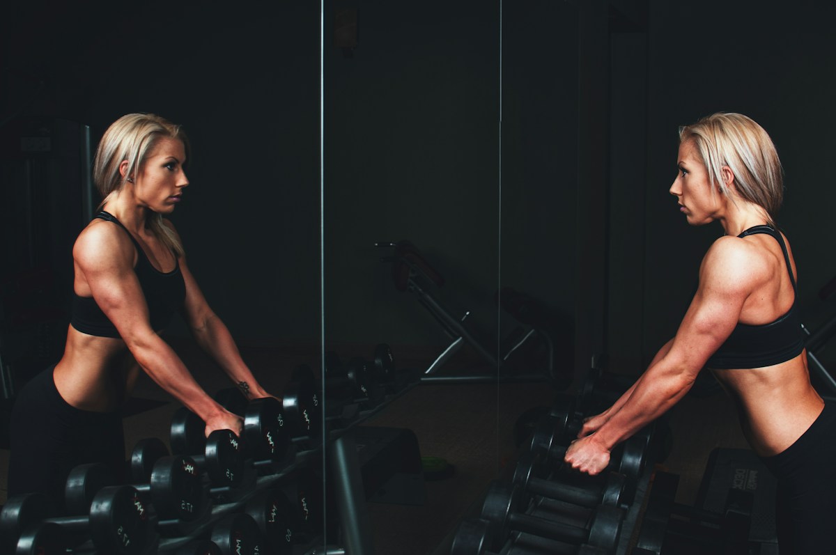 Femme musclée s’entraînant aux haltères devant un miroir