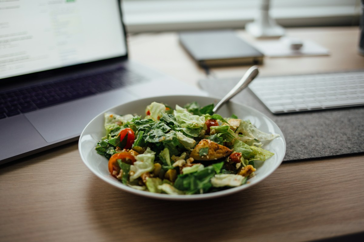 Salade composée dans un bol, entourée d’un ordinateur portable et clavier